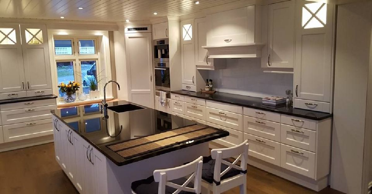 Stort, hvitt kjøkken med sorte benkeplater, kjøkkenøy og integrerte hvitevarer.